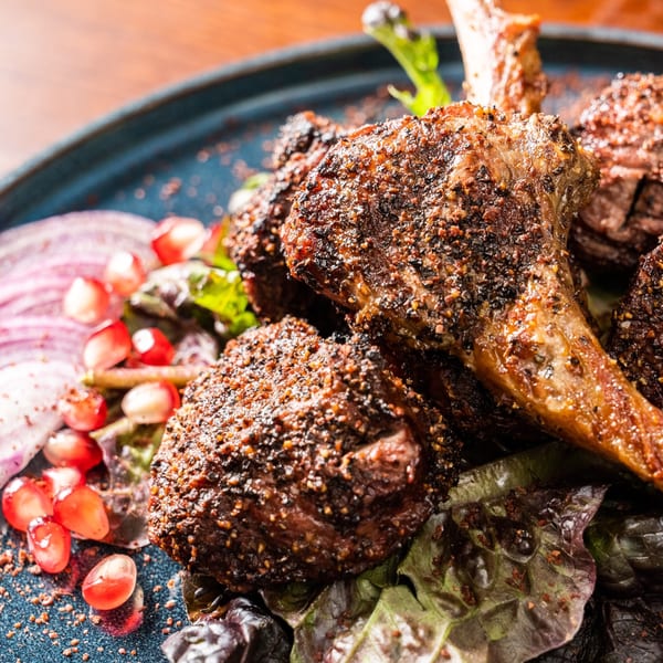 Close-up of Georgian lamb chops with pomegranate seeds, red onion, and greens on a blue plate.