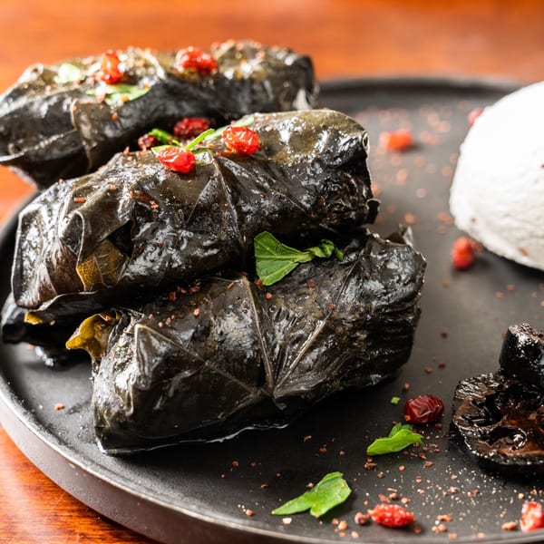 Georgian dolma, grape leaves stuffed with meat and rice, garnished with red berries and herbs.