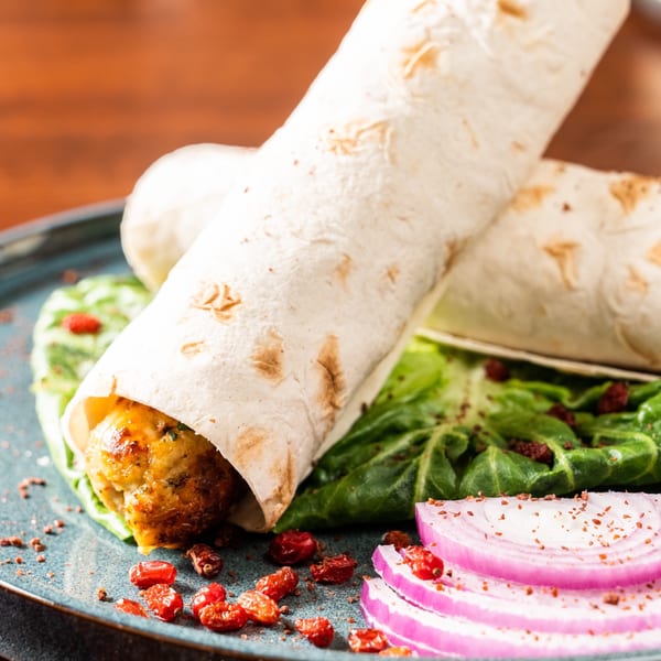 Two Georgian wraps with meat, lettuce, red onion, and dried berries on a blue plate.