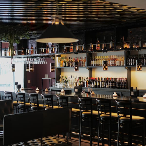 A long, dark bar with many bottles of spirits and wine, and bar stools.
