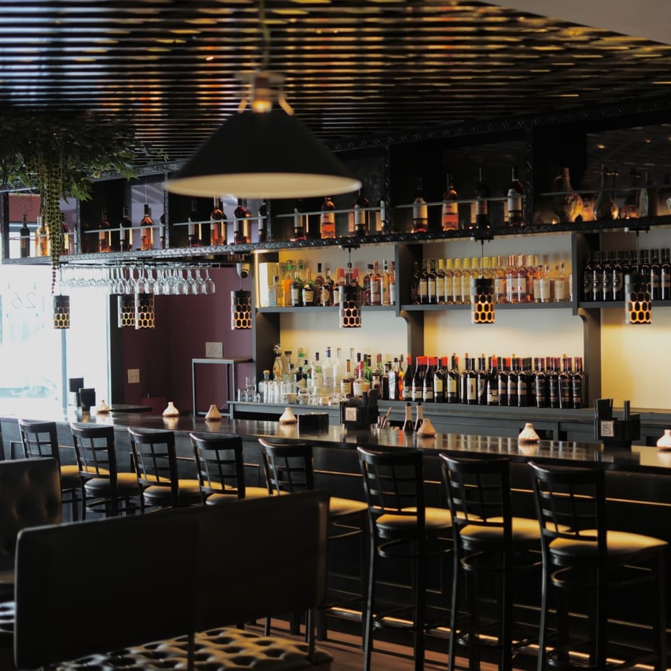 A long, dark bar with many bottles of spirits and wine, and bar stools.