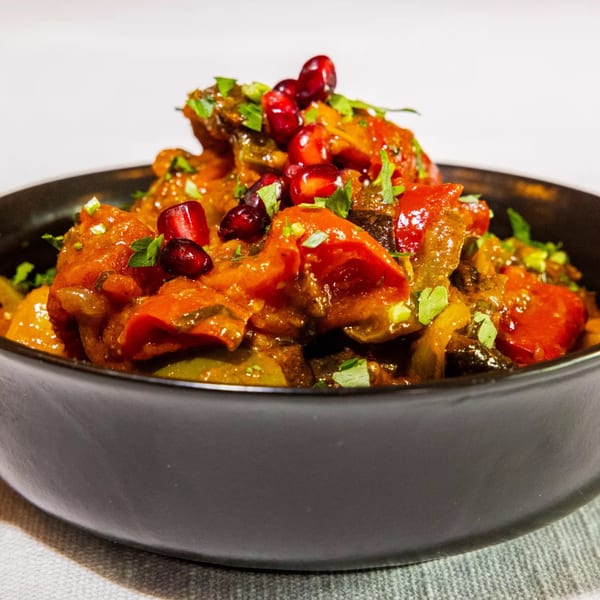 Badageoni's Georgian Ajapsandali, a vegetable stew with pomegranate seeds, in a black bowl.
