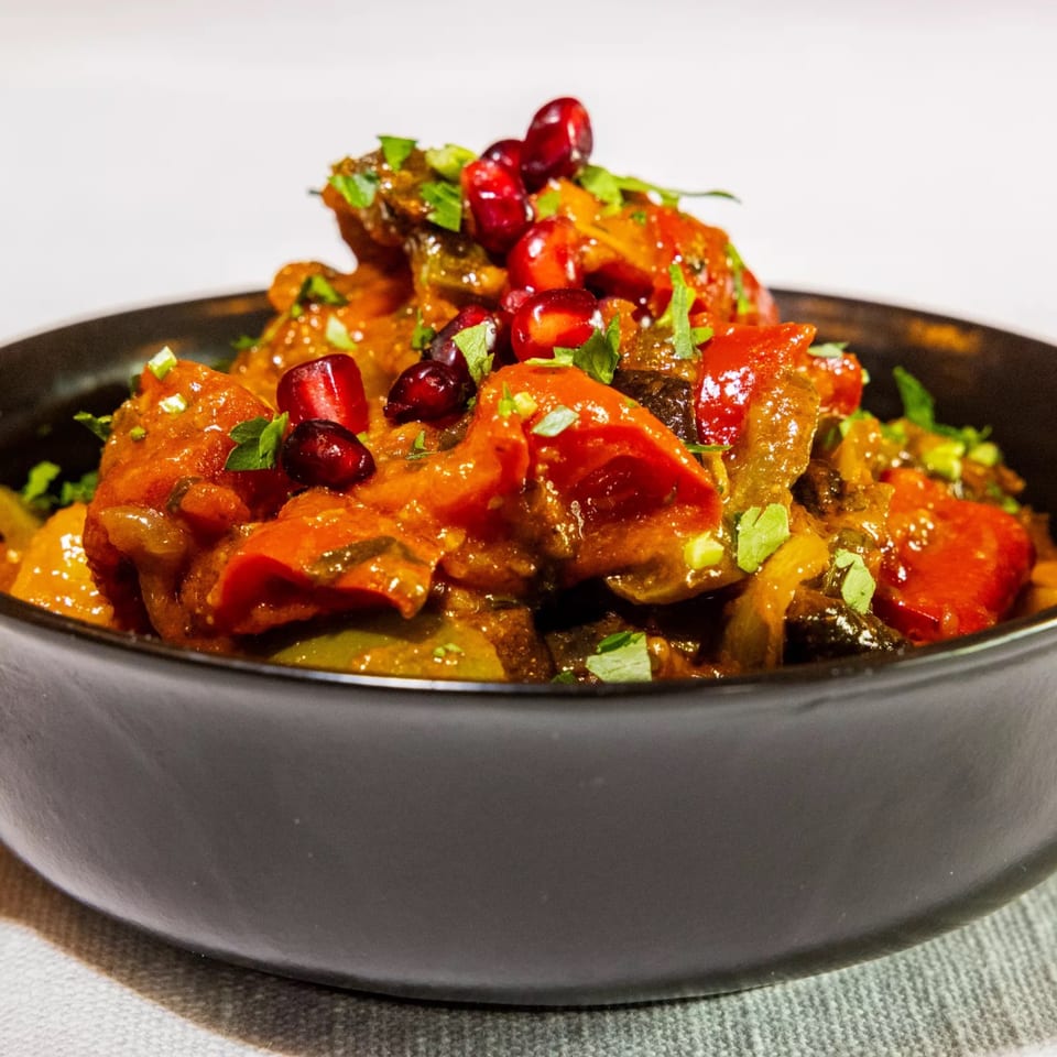 Badageoni's Georgian Ajapsandali, a vegetable stew with pomegranate seeds, in a black bowl.