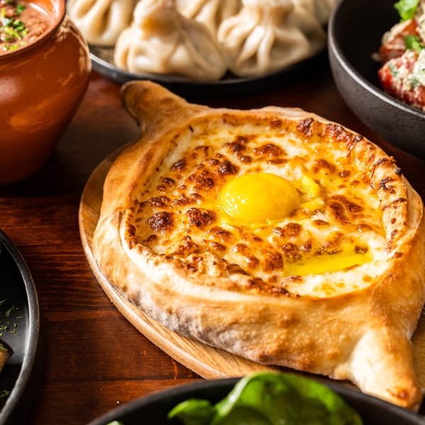 A close-up of a Georgian Adjaruli Khachapuri, a boat-shaped bread filled with melted cheese and a raw egg yolk.